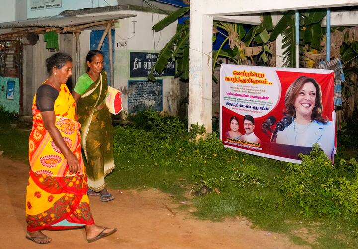 Women walk past a banner, asking people to join a special victory prayer for Democratic Presidential nominee Kamala Harris in the US election, at her ancestral village of Thulesendrapuram in Mannargudi district, Monday, Nov. 4, 2024. (Image Source: PTI)