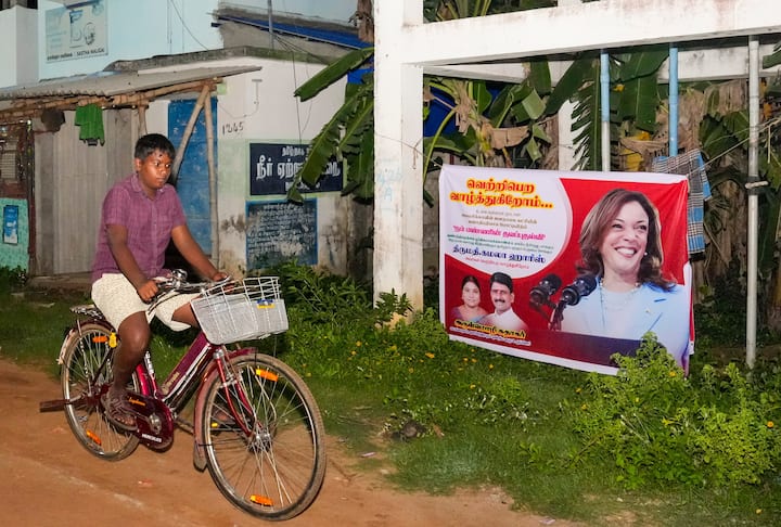 A cyclist rides past a banner, asking people to join a special victory prayer for Democratic Presidential nominee Kamala Harris in the US election, at her ancestral village of Thulesendrapuram in Mannargudi district, Monday, Nov. 4, 2024. (Image Source: PTI)