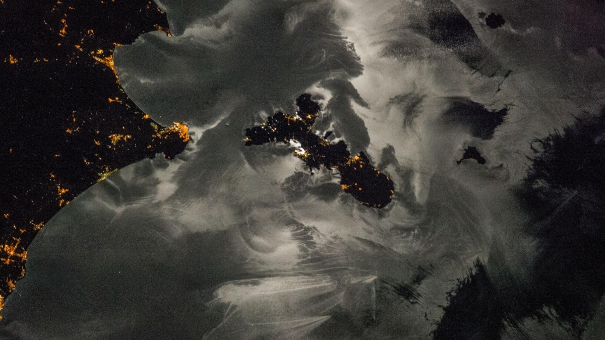 A nighttime view of Italy’s Elba island and surrounding towns showcases moon glint revealing sea surface patterns. City lights and dark sea areas blend in this stunning nocturnal image.