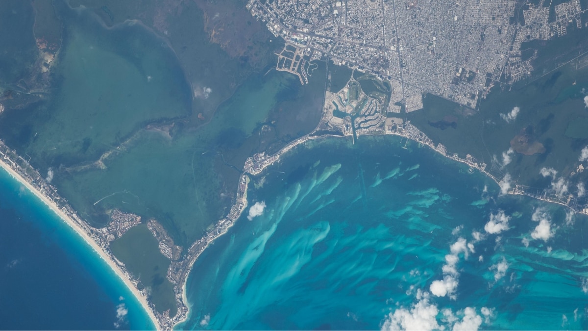 Cancún’s urban layout contrasts with its marinas and coral reefs. The image highlights vibrant blue waters, white sand beaches, and reduced wave energy along protected shorelines.