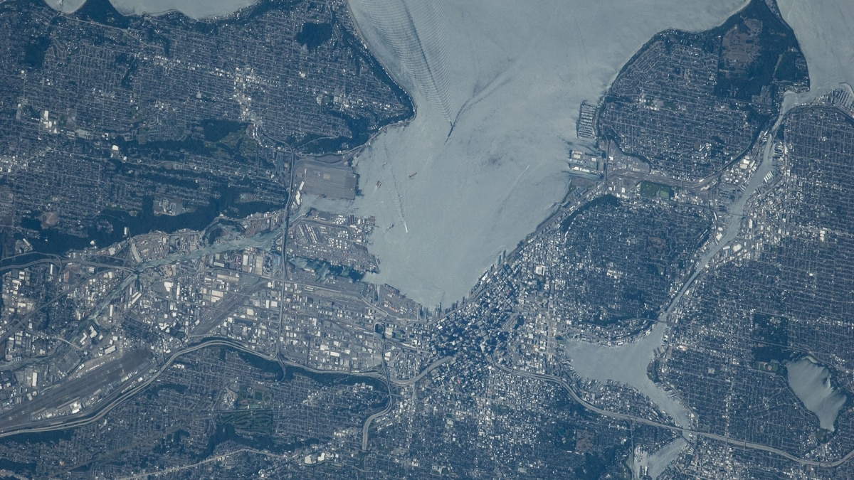 This detailed shot of Puget Sound reflects the sun, highlighting boat wake patterns and Seattle’s urban landscape. Tree-covered suburbs contrast with downtown shadows cast by high-rise buildings.