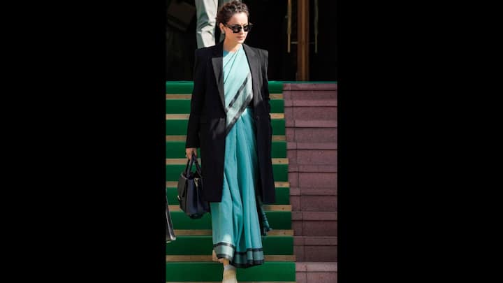 2. Sophisticated Look With Blue Saree: Kangana's blue saree with black borders give a simplistic vibe to the actress. She has paired her look with small earrings and black sunglasses. The jet black trench coat adds sophistication to the outfit and elevates the look. (Image Source: PTI)