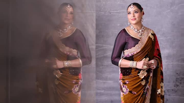 Bipasha turned heads in an eye-grabbing floral saree, which had a dramatic half-and-half cutting. The fabric of the saree was detailed with velvet and net, enhanced by delicate embroidery. With a serious bun, fresh flowers, a red bindi, and lovely diamond-ruby jewellery, it's a great look for those who want elegance for the evening. (Image Source: Instagram/ bipashabasu)