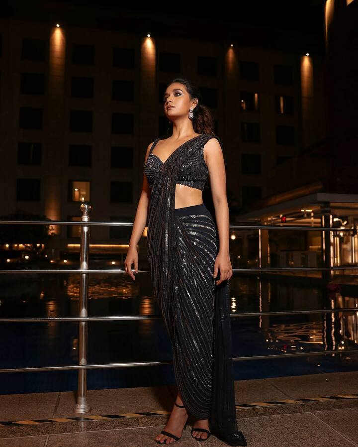 Keerthy stunned in a black saree featuring intricate work, paired with a sleeveless blouse and simple earrings, completing the look with a neat ponytail.