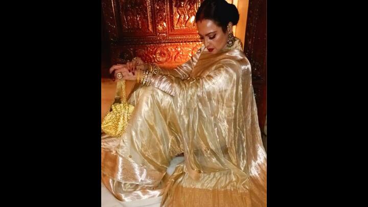 1. Rekha: Rekha epitomises regal charm in a golden handloom tissue saree. The actress has worn traditional jewellery and high block heels. Rekha has paired her iconic classic style with a matching potli bag and bold red lips. (Image Source: Instagram/@manishmalhotra05)