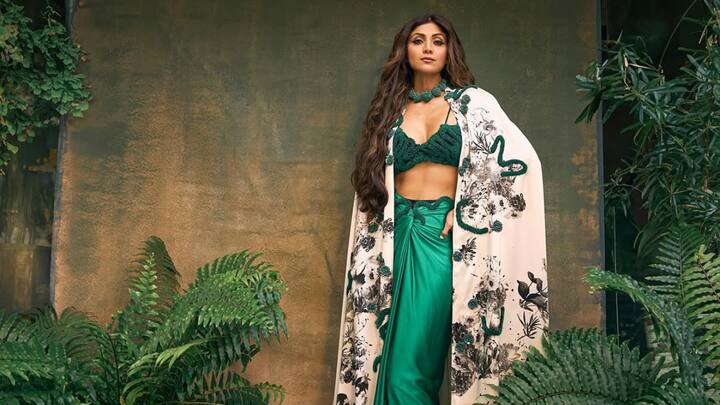 Shilpa Shetty's attire dazzled in a green three-piece co-ord set, paired with a white, printed, and classy cape thrown over the shoulder. Coupled with a striking chunky green choker necklace and very high-heeled shoes, her ensemble screamed the loudest style. (Image Source: Instagram/ theshilpashetty)