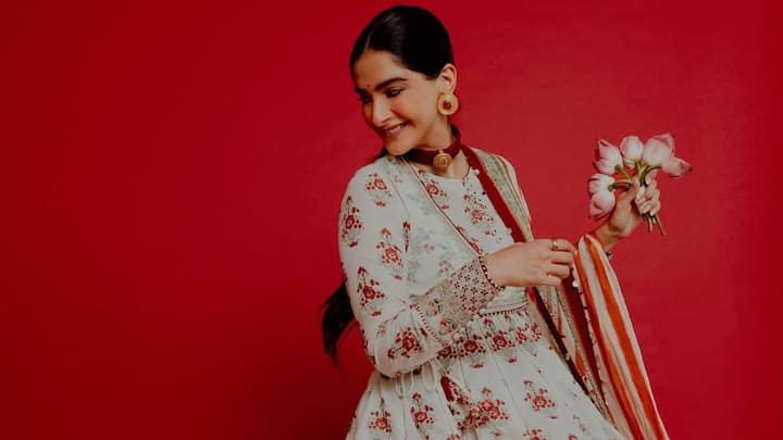 Sonam Kapoor mesmerised in a white Anarkali adorned with red and green floral prints. The outfit, paired with a matching jacket and dupatta, exuded traditional charm. Completing her with less makeup, red jewellery, and a striking red bindi, making it a flawless festive attire. (Image Source: Instagram/ sonamkapoor)