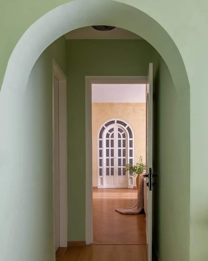 The arched entryway features a custom rattan mirror, a rustic black-framed wood bench, and warm decor elements.