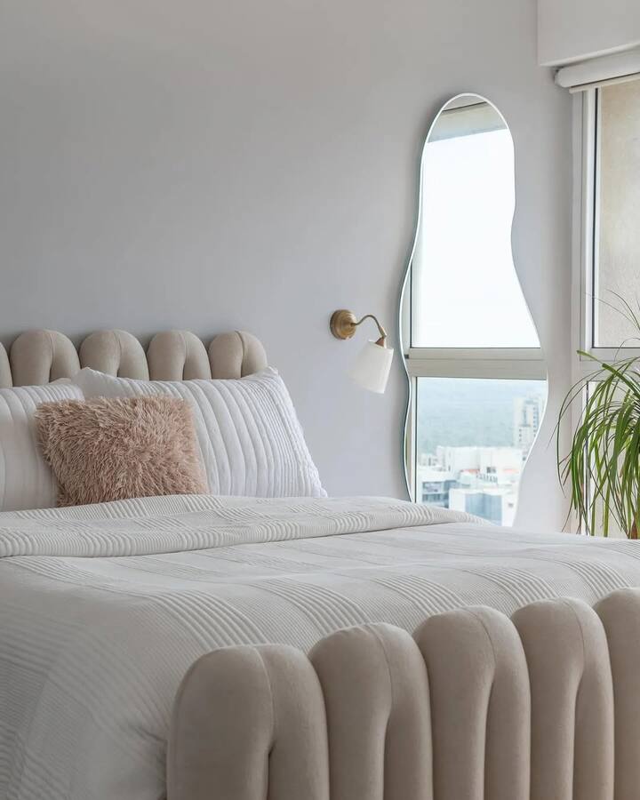 Aditi’s bedroom has a bold yellow curvilinear doorway, a custom serpentine-style upholstered bed, and a chic carpeted space.