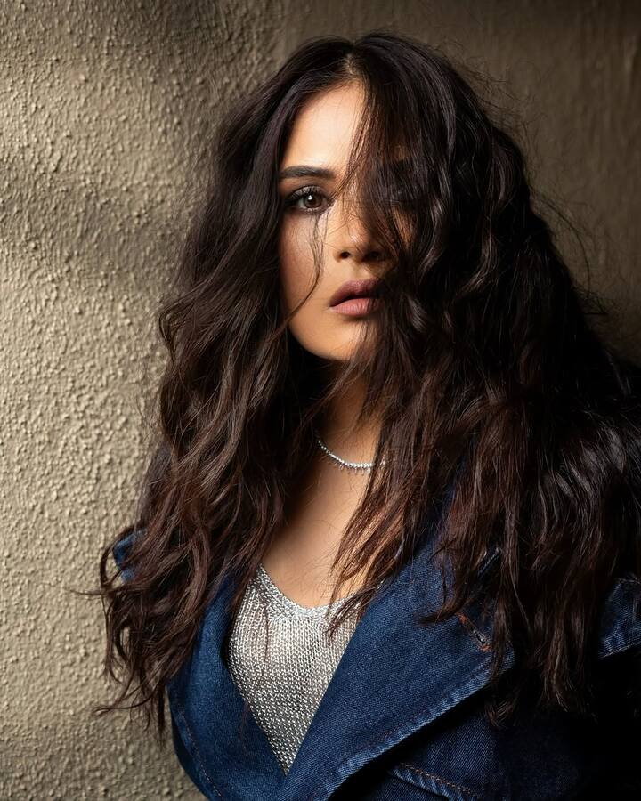 Richa’s long, voluminous curls cascade down her shoulders, giving her a fierce, untamed look. The loose, natural waves enhance the rawness of the denim, adding a sense of effortless beauty.