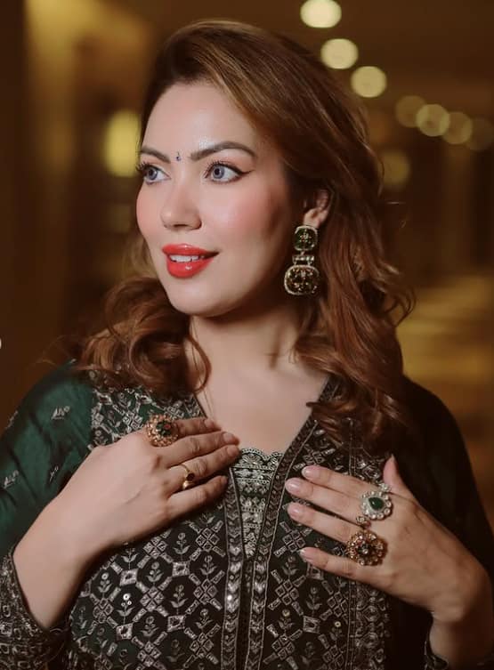 Munmun is wearing heavy earrings with his green suit and is also wearing many rings in both hands.