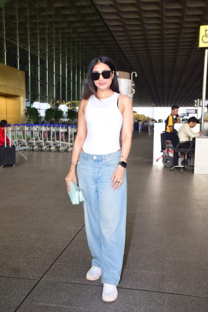 धनश्री वर्मा एयरपोर्ट पर स्पॉट हुईं. उन्होंने डेनिम के साथ व्हाइट टॉप कैरी किया हुआ था. उन्होंने अपने लुक को व्हाइट स्नीकर और ब्लैक शेड्स के साथ कंप्लीट किया.