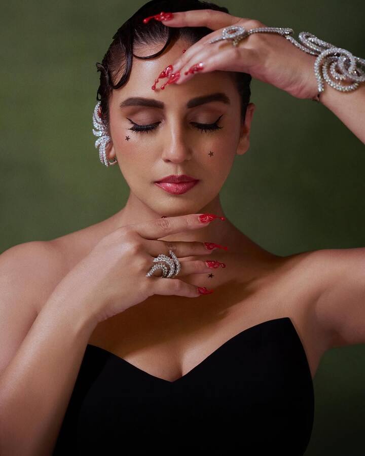 Her makeup was equally dramatic, with a dewy base, sculpted cheekbones, and a glossy nude-pink lip. The defining elements of the look were the tiny black star decals delicately placed on her cheeks and collarbone, adding a celestial charm.