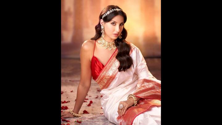 5. Nora Fatehi: Nora Fatehi looked dazzling in her red and white saree look. Her saree had golden zari work that gave her a unique look. The actress wore a noodle strap, deep V-neck blouse that blended traditional and modern styles. She opted for statement traditional jewellery that enhanced her look. (Image Source: Pinterest/famouspeopleindiaworld)