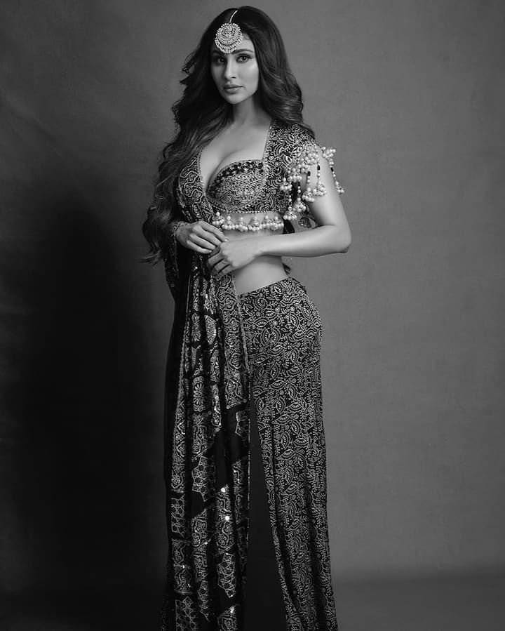 Mouni donned an intricately designed Ajrakh print lehenga set, featuring rich, earthy tones of black, gold, and rust red. The blouse boasted a bold plunging neckline with elaborate mirror work and delicate pearl tassels that added a dramatic flair to the traditional silhouette.