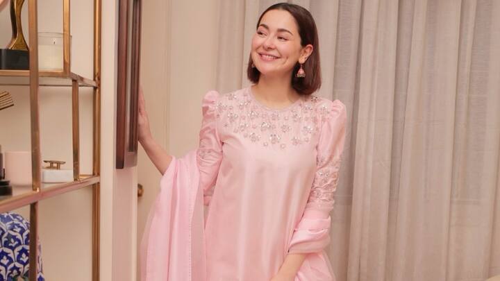 Draped in baby-pink raw silk, this hand-embellished suit complemented with a crystal-detailed dupatta is a pleasing pick for wedding festivities; the embroidered shalwar adds to its festive appeal. (Image Source: Instagram/ haniaheheofficial)