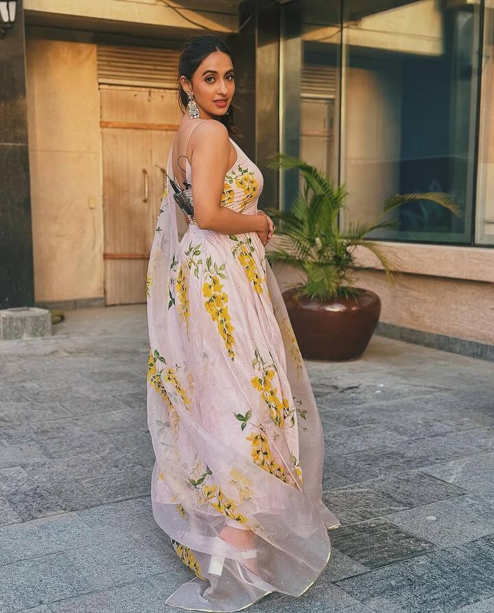 Akansha is dressed in a light lavender anarkali suit adorned with hand-painted yellow floral motifs. The soft, flowing fabric adds to the romantic appeal, and the matching dupatta, featuring the same floral accents, enhances the dreamy vibe. The silhouette is structured yet flowy, giving her an effortlessly graceful look.