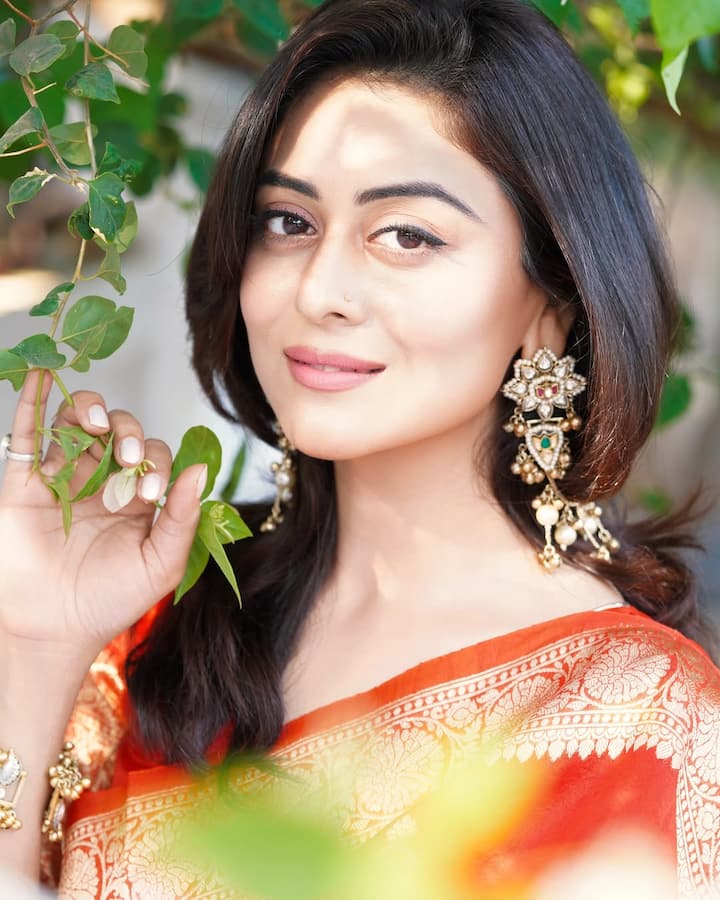 The color choice—a bold, warm orange—complements her glowing complexion and brings out a vibrant yet serene aura. Her look is traditional yet contemporary, a testament to her refined fashion sense that blends heritage with elegance.