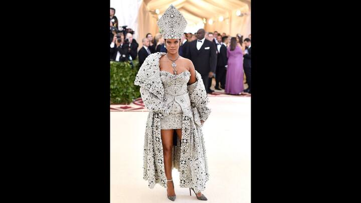 7. Rihanna: Rihanna turned the Met Gala into a moment of high fashion as she embraced religious iconography with elegance. She wore a cream hued and jewel encrusted gown that she layered under a heavily ornated overcoat. She completed her look with a statement headpiece, jewellery, and heels. (Image Source: Instagram/@wwd)