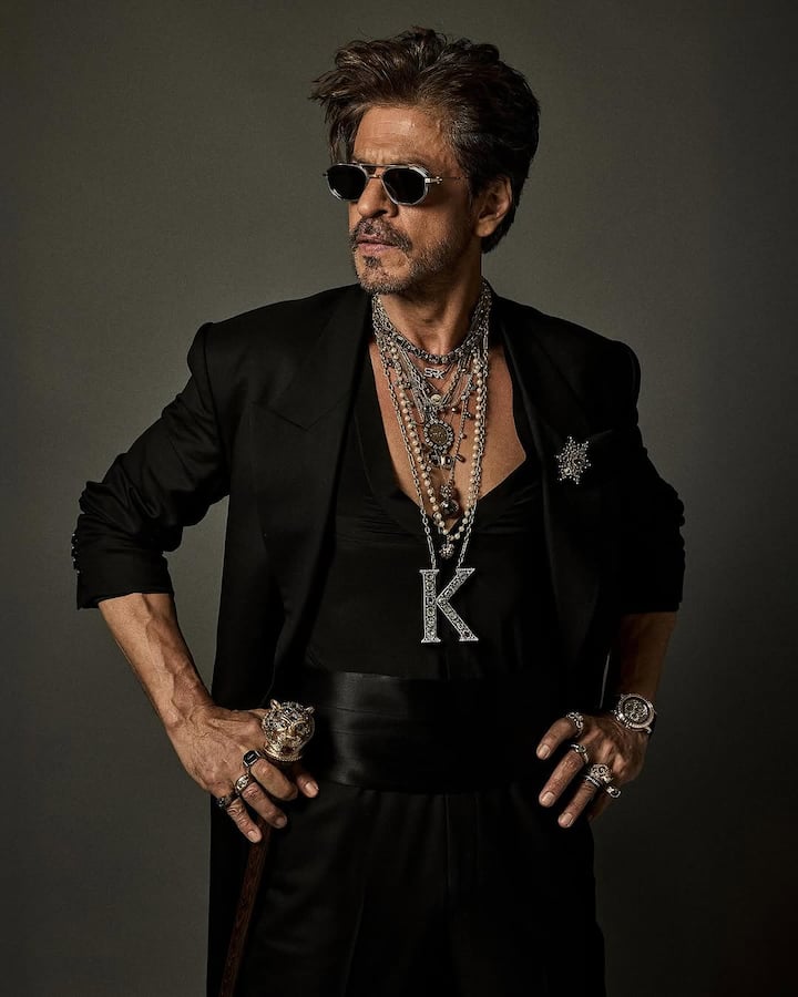 Shah Rukh Khan stunned in all-black Sabyasachi, accessorised with jewellery, dark shades, a cane, and a bold “K” pendant — exuding royal dandy energy. (Instagram/sabyasachiofficial)