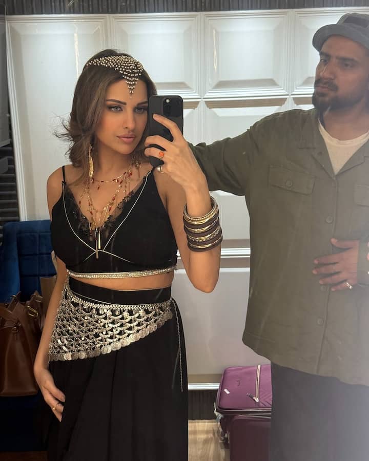 Himanshi donned a statement black outfit featuring a strappy crop top with delicate lace accents and a flowy skirt. The standout element was the metallic silver waist belt with cascading coin detailing, reminiscent of traditional belly-dancer attire, adding a boho-glam flair to the ensemble. The silhouette flattered her figure while allowing ease of movement—perfect for a dance shoot.