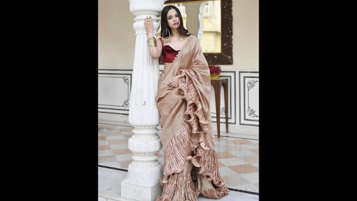 8. Ruffled Saree: The luxurious champagne-toned saree with dramatic ruffle detailing along the hem and pallu gave Nitanshi Goel a timeless charm. The pleated texture of the ruffles added volume and gave the traditional fit a modern touch. The saree had a metallic sheen which enhanced its grandeur. For a contrasting look, Nitanshi paired the saree with a deep maroon blouse. The accessoried her look with statement gold earrings and chunky bangles. (Image Source: Instagram/@nitanshigoelofficial)