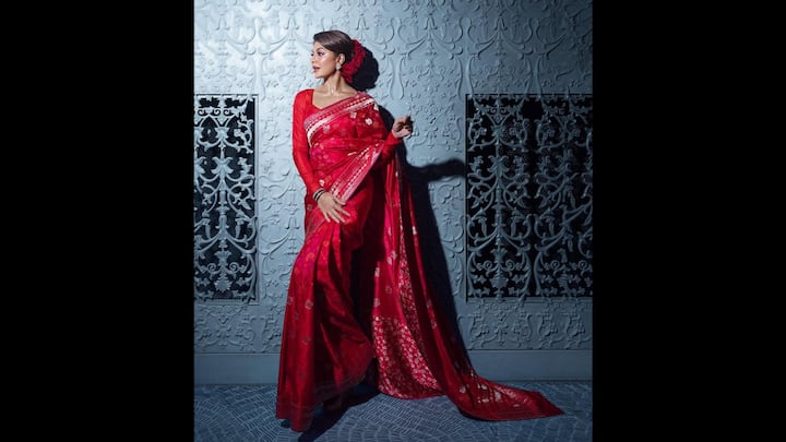 4. Ravishing Red Saree: The striking red saree worn by Jacqueline Fernandez gave the actress a beautiful ethnic look. She wore a full-sleeved blouse that added traditional grace. The saree had silver embroidery all over it which enhanced the traditional ensemble's overall appeal. The actress opted for minimal jewellery and red roses pinned into her sleek updo. (Image Source: Instagram/@jacquelienefernandez)