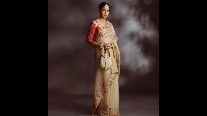 1. Traditional Beige Saree: Genelia D'Souza exuded timeless elegance is a tradition saree that was refined with glamour. The sheer beige saree was adorned with delicate floral embroidery and sequin work along the borders, enhancing its grace. She wore a contrasting red blouse of a rich hue that had intricate zardozi embroidery. To create a masterpiece, she paired her saree with a statement maang tikka, pearl drop earrings, and stacked bangles along with a matching potli bag. (Image Source: Instagram/@geneliad)