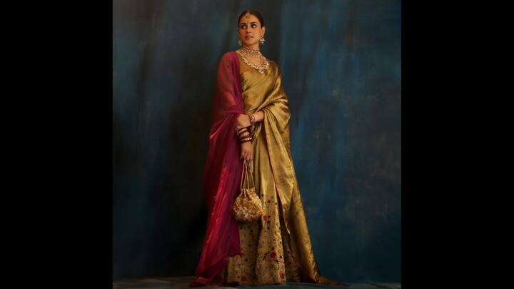 4. Classic Gold Drape: Genelia D'Souza opted for a timeless and charming exquisite saree. The rich golden saree had a muted sheen and classic weave that embodied sophistication. She added a magenta dupatta for a bold and contrasting look that elevated the regal tone. The actress accessorised her statement look with a dazzling choker, statement earrings, and a matha patti. She finished her look with classic gold and red bangles and traditional red bindi. (Image Source: Instagram/@geneliad)