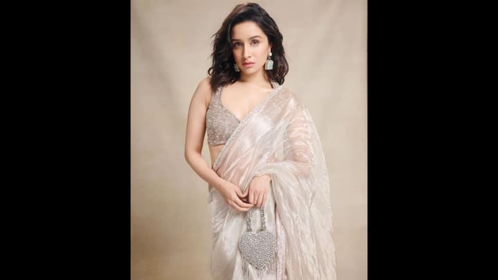 1. Shraddha Kapoor wore a pastel saree with a lustrous sheer fabric that exuded sophistication. The delicate shimmer and texture enhanced the festive appeal of the ethnic look. She added a sleeveless blouse which was heavily embellished with embroidery and sequins for a touch of glamour. The actress paired her look with a heart-shaped embellished bag which gave a chic look and statement earrings which complemented the mute tones of the fit. (Image Source: Twitter/@hajarkagalwa)