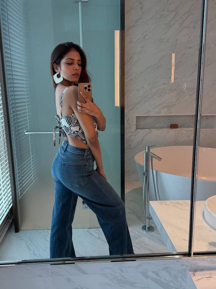 She pairs it with high-waisted, wide-leg blue jeans that lend a vintage flair and balance the edgy top with a classic silhouette. The denim not only elongates her frame but also cements the 'cool-girl on vacation' aesthetic she channels.