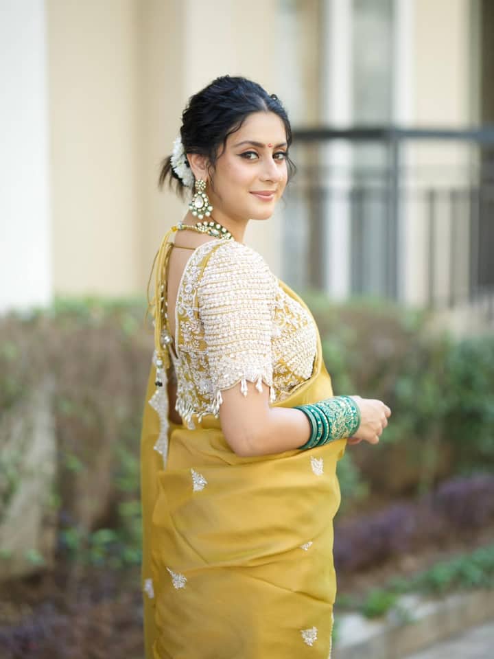 Her hair is styled in a soft updo, adorned with fresh white flowers at the back for a touch of timeless grace.