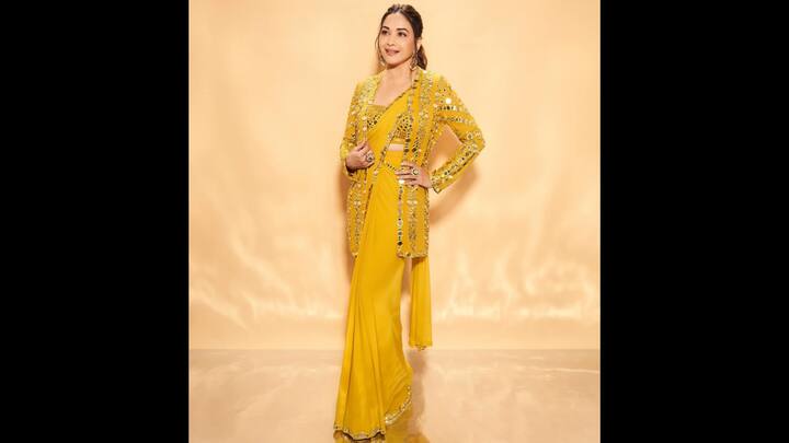 8. Madhuri Dixit: Madhuri Dixit turned heads in a radiant mustard yellow saree, elevated with intricate mirror work that brought a glamorous edge to traditional wear. The saree featured minimalistic drapes with a sleek silhouette, perfectly paired with a heavily embellished blouse and a long mirror work jacket that doubled the dazzle. With its bold placement of reflective detailing, the jacket offered a striking contrast, giving the entire outfit a contemporary twist while staying rooted in Indian craftsmanship. Her choice of softly tied hair, radiant makeup, and minimal jewellery allowed the statement ensemble to shine. (Image Source: Instagram/@madhuridixitnene)