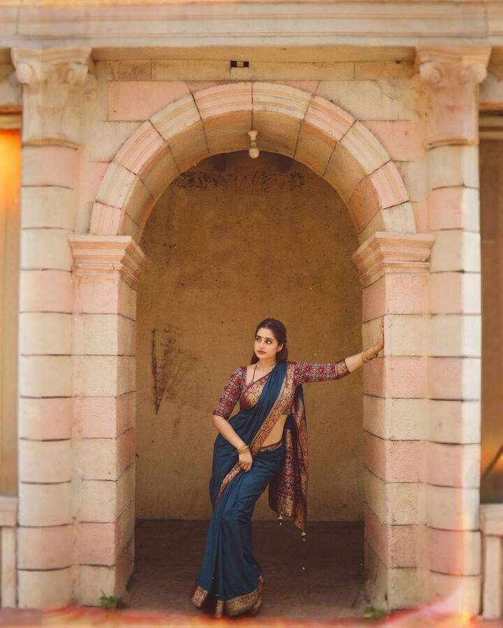 Ayesha stuns in an opulent teal saree adorned with an intricately woven maroon floral border.
