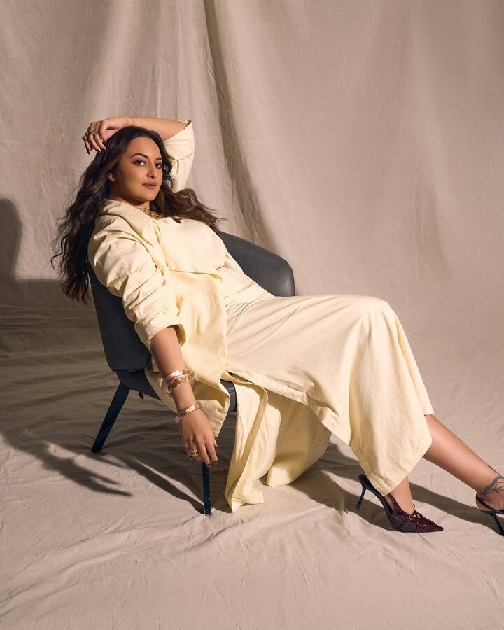 Layered over the dress was a relaxed, longline jacket in the same shade, giving her ensemble a dreamy, fluid structure. The look was cinched at the waist with a tan belt, adding definition and a touch of earthy contrast to the otherwise all-ivory palette.