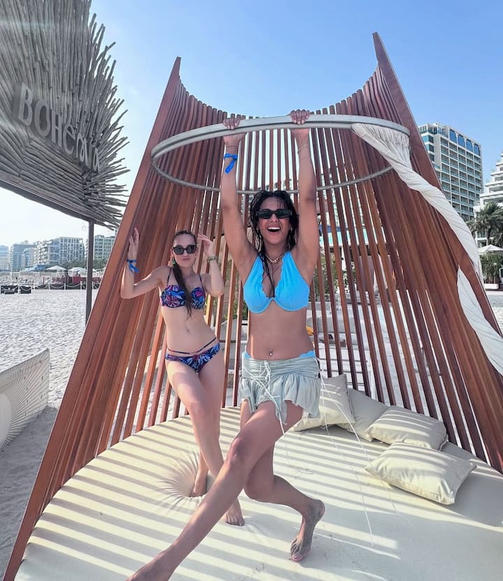 Nia struck a fun pose hanging from a chic wooden structure by the beach.