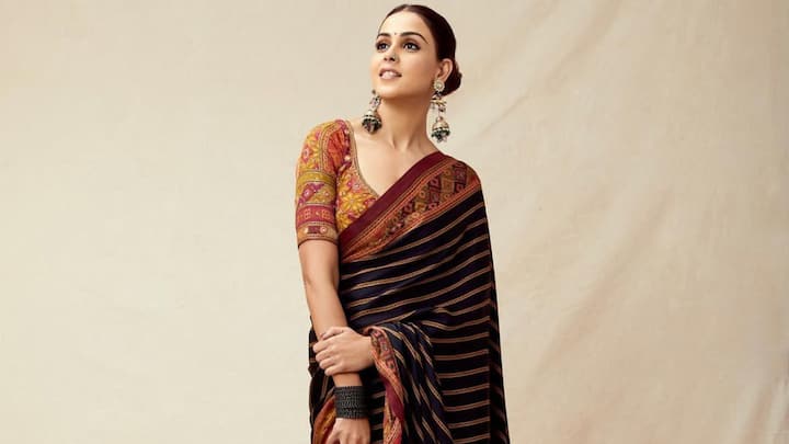 Genelia looks radiant in this black hand-painted silk saree with rusty orange stripes and wide multicoloured borders. Worn with an intricately embroidered blouse, this outfit is ideal for evening celebrations. (Image Source: Instagram/ geneliad)