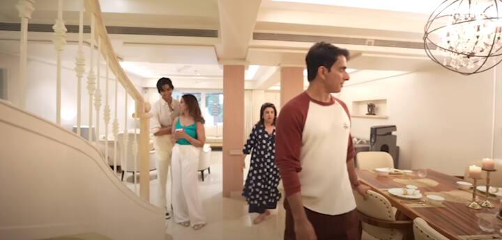 The living room is bright, airy, and elegant with white and beige interiors, a stylish sofa set, lamps, and a centrally placed staircase.