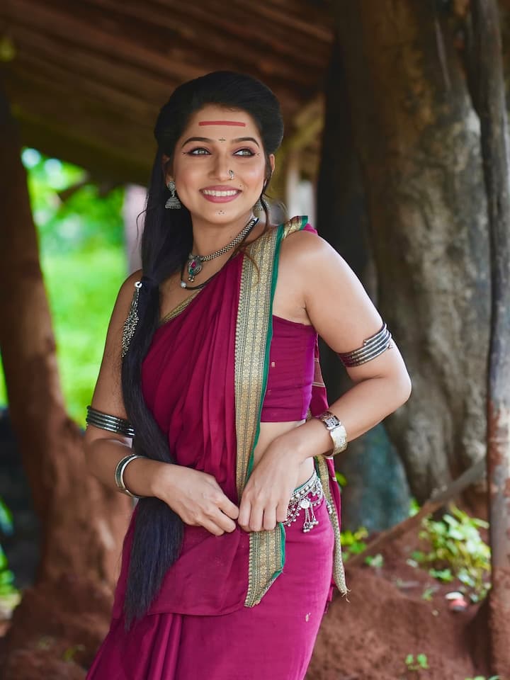 तिने गडद जांभळ्या रंगाची सोनेरी काठाची नऊवारी साडी परिधान केली आहे, जी पारंपरिक मराठी सौंदर्याची ओळख आहे.