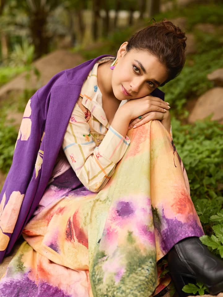 Beneath the jacket, a flowy watercolour dress peeks through, an abstract blend of sunset tones and forest greens.