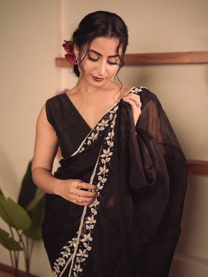 Aishwarya Sharma stands confidently against a simple backdrop, allowing her black saree to be the focus.