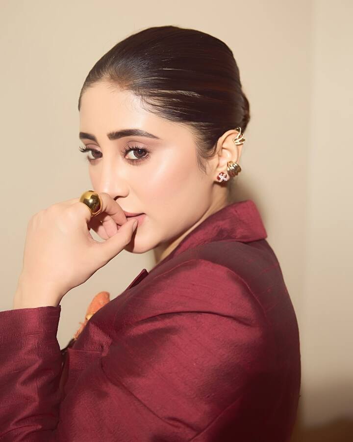 Her sleek bun accentuates the structure of her face, while the oversized gold ring and sculptural ear cuffs add a touch of bold elegance.