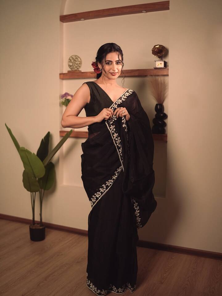 The black chiffon saree falls elegantly along her frame, with a sheer texture that adds softness to the look.