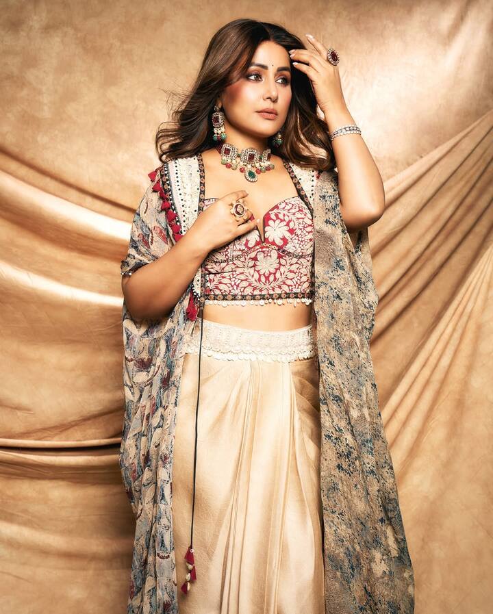 Hina has carried a beautiful fusion look. She is wearing a golden satin drape-style skirt, which has been styled like a saree. With this, he is wearing a deep neck embroidered blouse. From above, she is wearing a flowi cape-style shrug, in which the velvet pattern and the tussle detailing look are elevating even more.