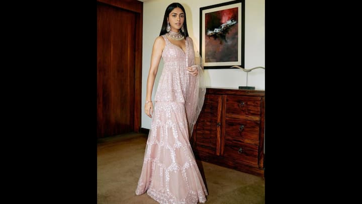 1. Blush Pink Sharara Set: Mrunal Thakur served major festive fashion inspiration with this dreamy blush pink Sharara set. The outfit features intricate sequin embroidery that gave the ethnic fit a contemporary vibe. The deep V-neckline added a touch of modern elegance to the traditional fit. The matching sheer dupatta draped delicately over her shoulder elevated the overall grace of the look. Mrunal’s choice of jewellery made her outfit stand out. She wore an oversized choker and statement earrings that balanced the simplicity of her soft pink sharara set. (Image Source: Pinterest/HelloMoonlight_)