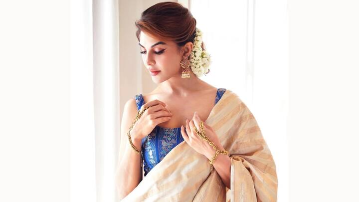 Draped in this handwoven beige silk saree with intricate gold detailing, Jacqueline elevates the look with a royal blue brocade corset adorned with floral embroidery. (Image Source: Instagram/ jacquelienefernandez)