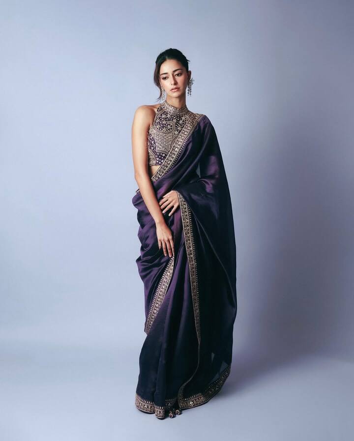 Ananya is wearing a Royal Purple Sari in her elegant look, on which the golden embroidery has done and has a halter-neck blouse. Statement earrings, soft makeup and sleek tie-up hairstyle is making this look more elegant.