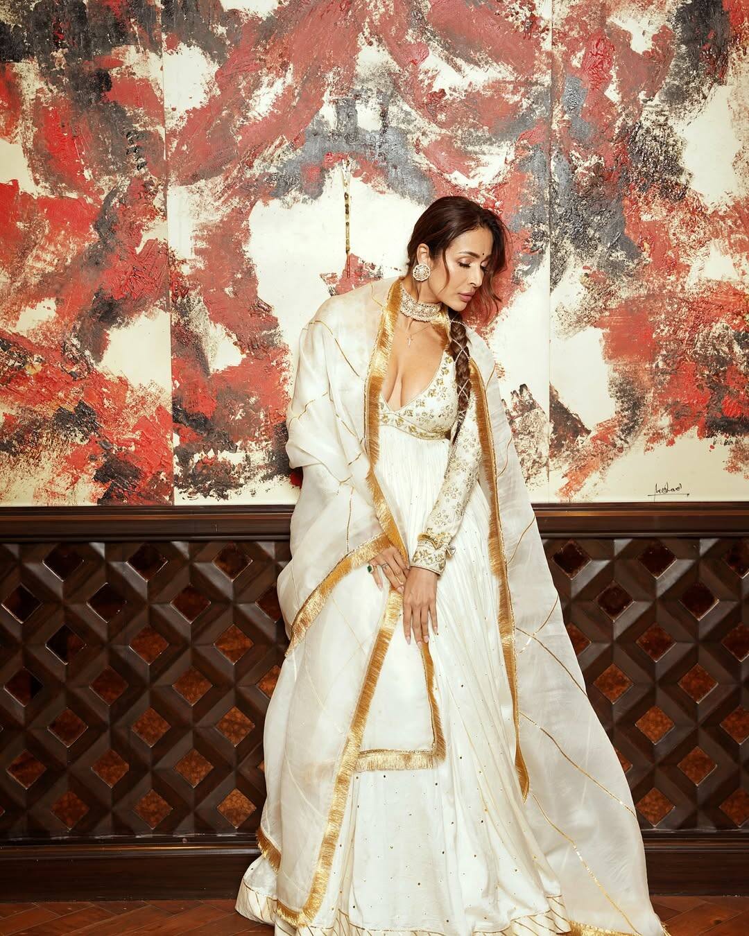 In this look, Malaika is wearing a beautiful white ethnic outfit with golden colored detailing, with which she is wearing a golden border matching scarf. Finely embroidered deepne blouse is giving a modern touch in this traditional outfit. He has made statement earrings, a bran and a sleek bread with it.