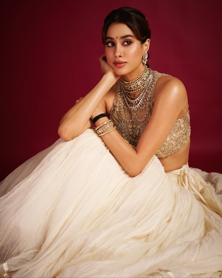 इस लुक में जान्हवी ने गोल्डन वर्क वाला हैवी ब्लाउज़ और ऑफ-व्हाइट फ्लोई लहंगा पहना है. गले में हैवी स्टेटमेंट ज्वेलरी, चूड़ियाँ और ईयररिंग्स उनके  लुक को और रिच बना रहे हैं. हल्का ग्लोइंग मेकअप, बिंदी और क्लासी हेयरस्टाइल उनके लुक को पूरा कर रहा है.