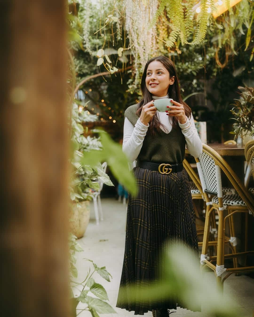In this picture, Shahnaz is wearing an olive green sweater above the white top and pair it with a black belt and a check -in pleated skirt. Complete the look with open hair and natural makeup.